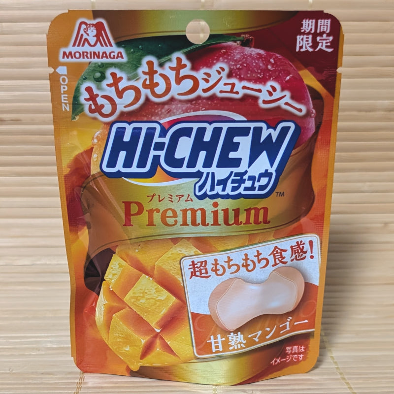 A gold and orange resealable pouch of Hi-Chew Premium Mango showing a cross-section of a soft candy and fresh mango, on a traditional Japanese tatami background.
