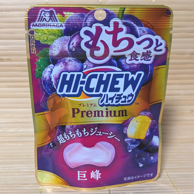 A metallic gold and purple 32g pouch of Morinaga Hi-Chew Premium Kyoho Grape showing deep purple grapes and a cross-section of a bouncy round candy on a bamboo mat background.