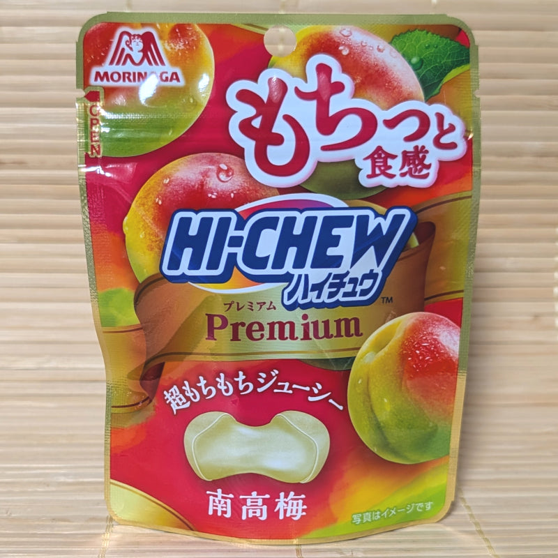 A metallic gold and red 32g pouch of Morinaga Hi-Chew Premium Kishu Nanko Ume showing ripe plum illustrations and a cross-section of a bouncy round candy on a bamboo mat background.