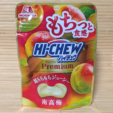 A metallic gold and red 32g pouch of Morinaga Hi-Chew Premium Kishu Nanko Ume showing ripe plum illustrations and a cross-section of a bouncy round candy on a bamboo mat background.