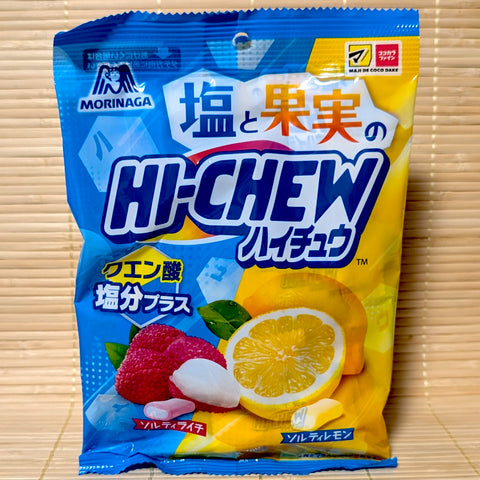 A blue and yellow split bag of Morinaga Hi-Chew Salty Lychee and Salty Lemon showing fresh sliced fruits and drugstore logos on a tatami background.