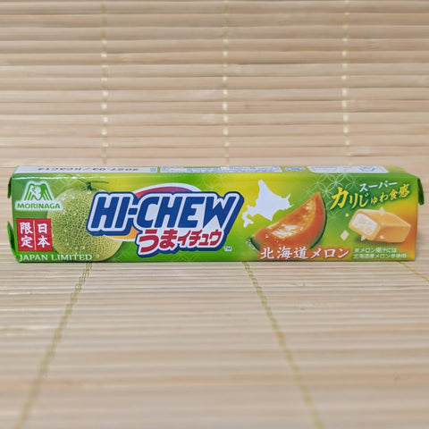 A green and orange stick of Japan Limited Morinaga Hi-Chew Umaichu Hokkaido Melon showing a cross-section of candy with crunchy crystals on a tatami background.