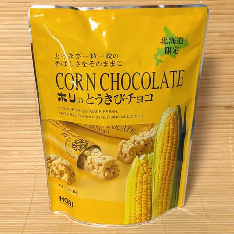 A yellow 100g stand-up pouch of Hori Corn Chocolate featuring sweet corn cobs and individual chocolate crisp bars on a bamboo mat.