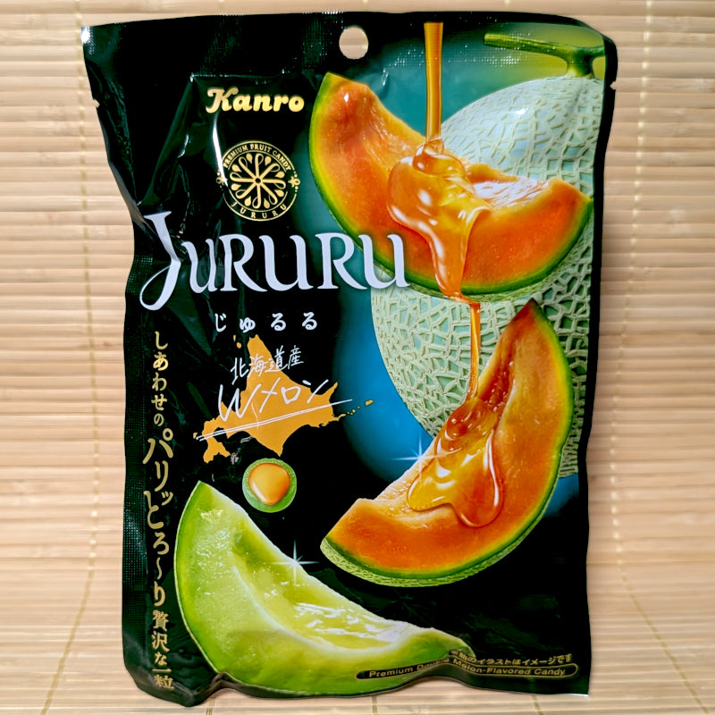 A sleek black 60g bag of Kanro JURURU Hokkaido Double Melon hard candy showing dripping melon gelee, sliced orange melon, sliced green melon, and a cross-section of the candy on a bamboo mat background.