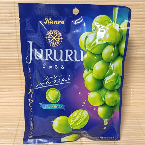 A deep blue bag of Kanro JURURU Shine Muscat candy showing a bunch of green grapes and a cross-section of a candy with a liquid center, on a tatami background.