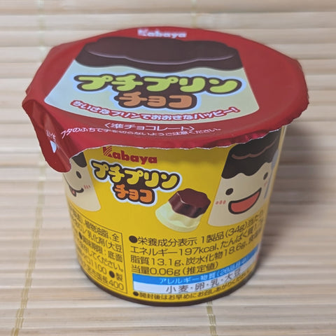 A small yellow and red Kabaya Petit Purin chocolate cup with a peel-off foil lid on a bamboo mat background.   