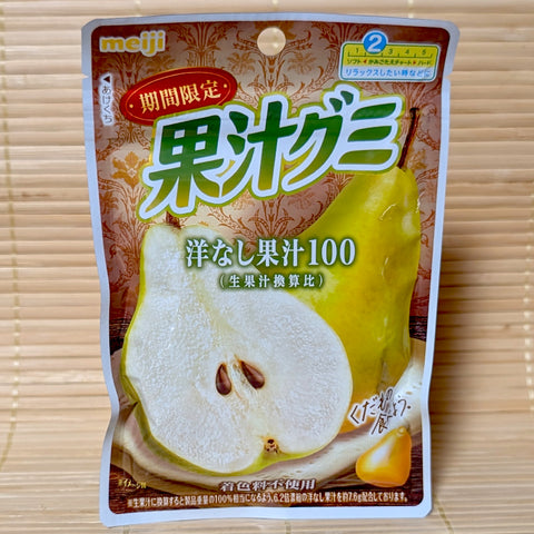 A packaging pouch of Meiji Kaju Gumi Western Pear gummies displaying a sliced green pear and the 100% fruit juice label on a bamboo mat background.