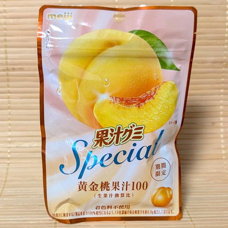 A metallic rose-gold pouch of Meiji Kaju Gummy Special Golden Peach showing a large sliced yellow peach on a tatami background.