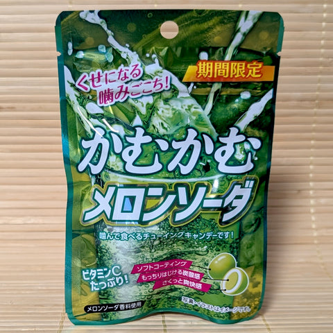A green resealable pouch of Kamu Kamu Melon Soda candy featuring a bubbly soda glass graphic and a cross-section of the chewy candy, on a tatami background.