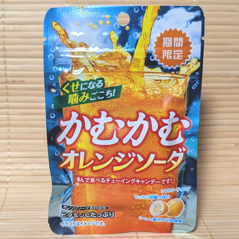 A bright blue and orange 30g pouch of Kamu Kamu Orange Soda candy showing a sparkling glass of orange soda and a cross-section of a chewy candy on a bamboo mat background.
