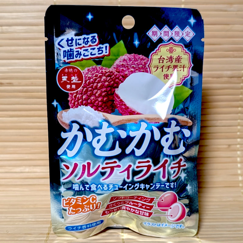 A deep blue and gold 30g resealable bag of Kamu Kamu Salty Lychee chewy candy showing whole lychee fruits and a spoonful of sea salt on a tatami background.