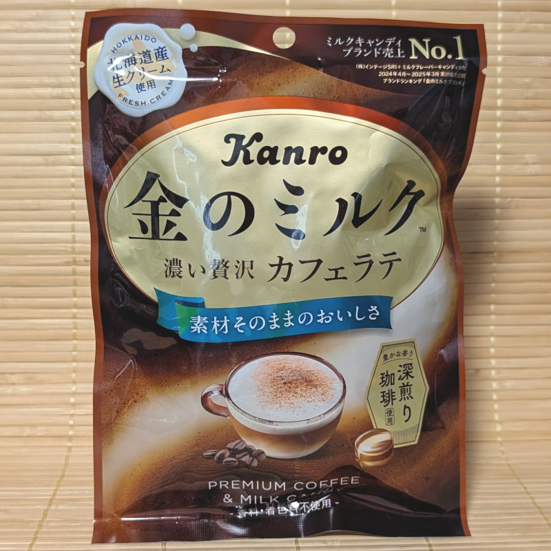 A gold and deep brown 61g bag of Kanro Golden Milk Cafe Latte hard candy displaying a creamy latte cup and coffee beans on a bamboo mat background.