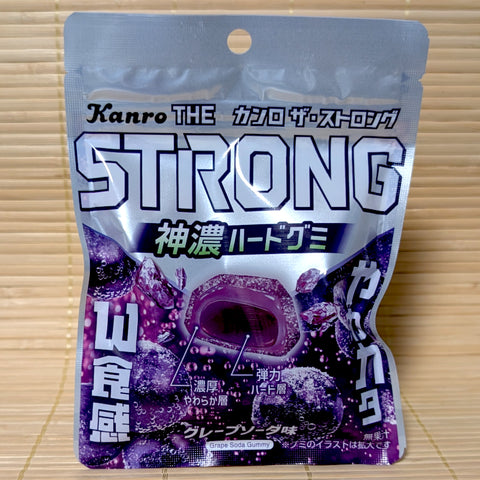 A silver and purple resealable pouch of Kanro THE STRONG gummies featuring a cross-section of the double-layer gem-shaped grape soda gummy.