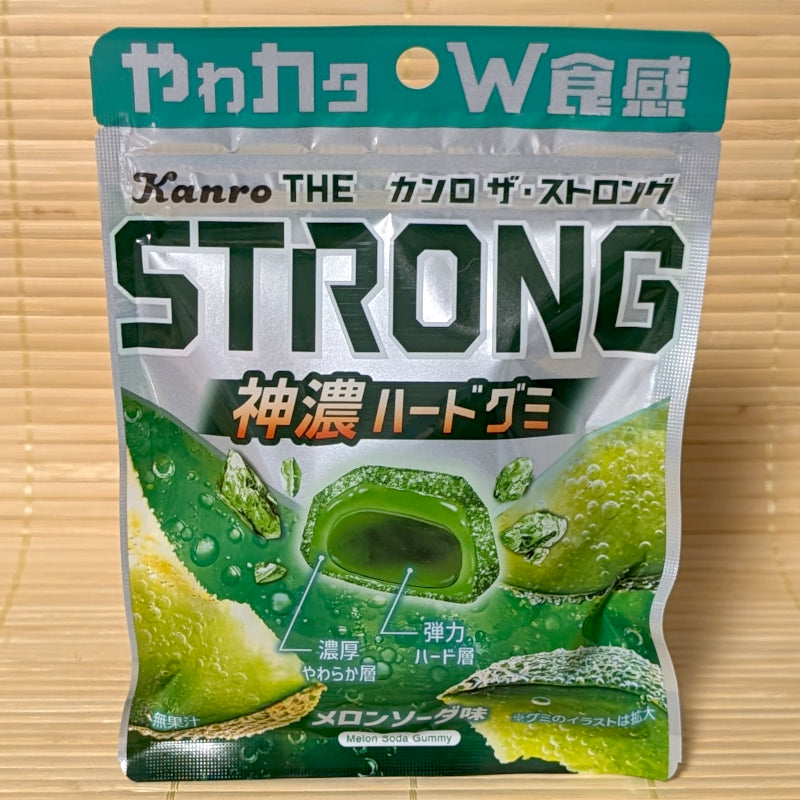 A pouch of THE Strong Melon Soda Gummy showing cross-section graphic of the dual-layer soft and hard texture, resting on a bamboo mat.