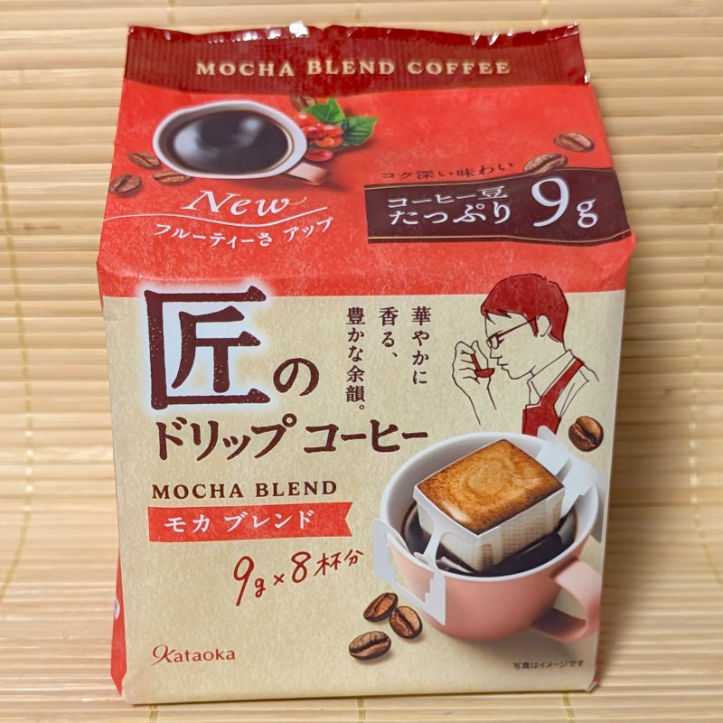 A red and white 72g package of Takumi Drip Coffee Mocha Blend showing a mug with a clip-on drip filter on a bamboo background.   