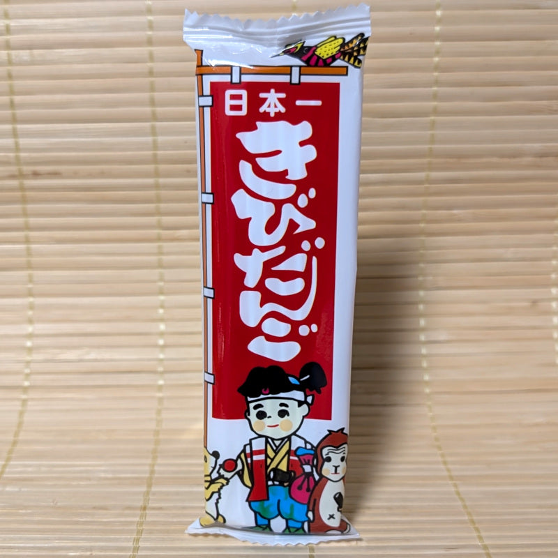 Japanese Kibi Dango dagasi snack package with cartoon Momotoro character. Displayed on a bamboo mat background.