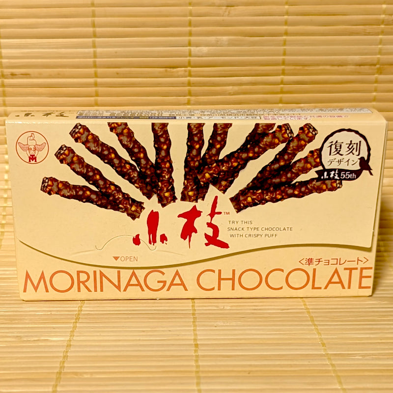 A retro-styled 55th anniversary box of Morinaga Koeda Classic Chocolate Twigs showing twig-shaped chocolates on a bamboo background.   