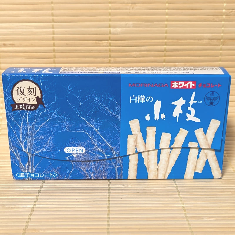 A blue 55th anniversary box of Morinaga Shirakaba Koeda White Chocolate Twigs showing white birch tree graphics on a bamboo background.