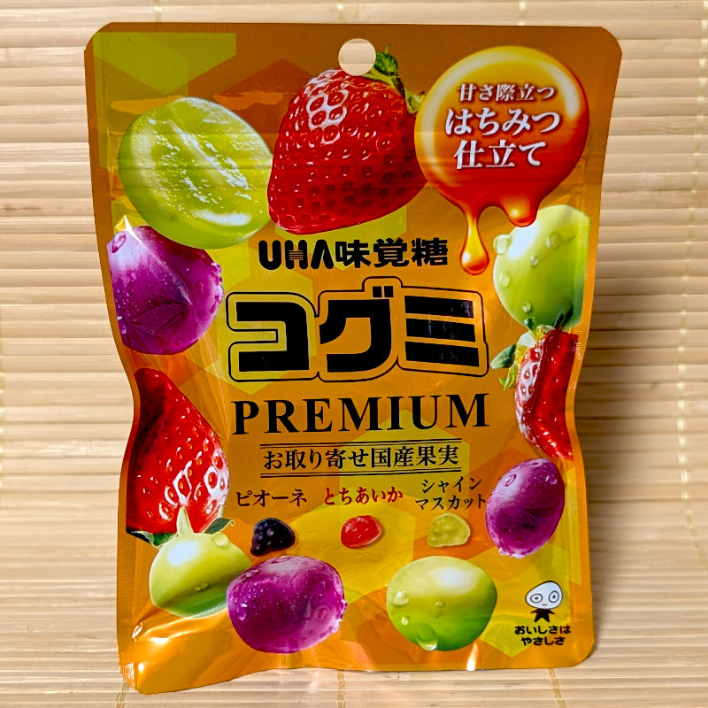 A golden yellow 75g pouch of Kogumi PREMIUM Japanese Honey Fruit Mix showing strawberries, grapes, and mini fruit gummies on a bamboo background.   