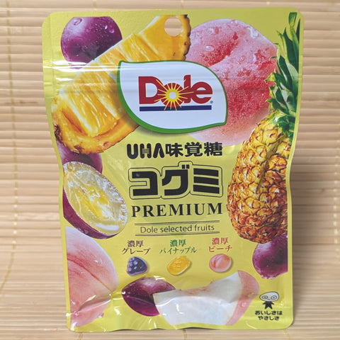 A yellow resealable UHA Kogumi bag on a tatami background with large photos of grapes, pineapple, and peaches next to the Dole logo.