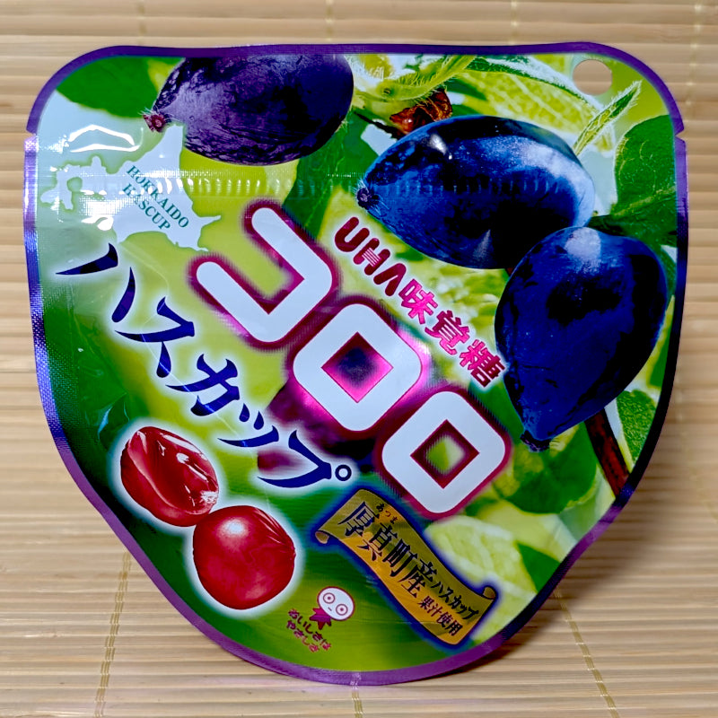 A bright green and purple heart-shaped pouch of UHA Kororo Hascap gummy showing large blue honeysuckle berries and a map of Hokkaido on a tatami background.