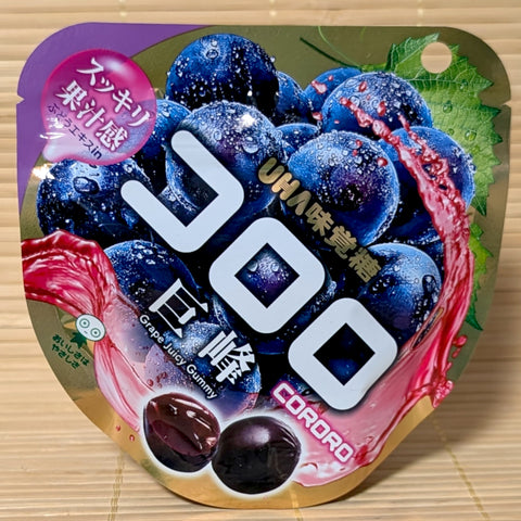 A purple and gold pouch of UHA Kororo Kyoho Grape Juicy Gummy featuring fresh grape graphics on a bamboo background.   