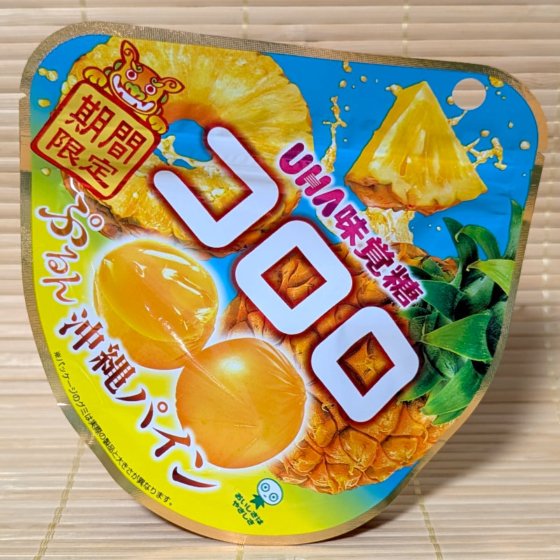 A unique curved blue and yellow beach-themed pouch of UHA Kororo Pineapple gummy candy showing fresh fruit graphics on a tatami background.
