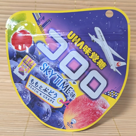 A purple and yellow pouch of UHA Kororo JAL Sky Time Peach and Grape gummies featuring a Japan Airlines plane.