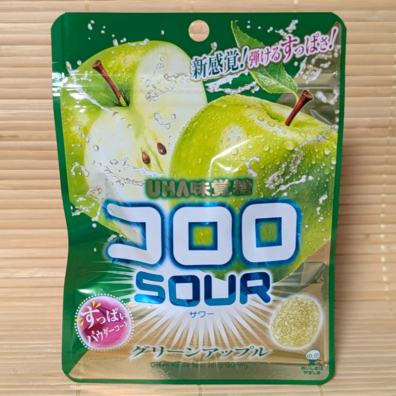 A vibrant green 45g pouch of UHA Kororo Sour Green Apple Gummies featuring crisp green apples and sour powder graphics on a bamboo mat background.