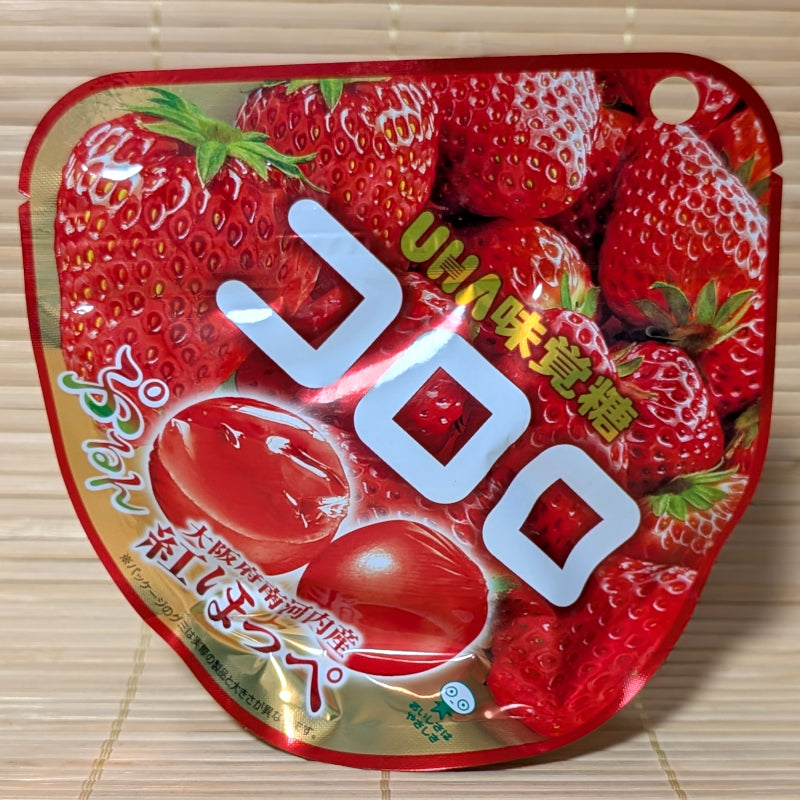 A bright red 40g pouch of UHA Kororo Minamikawachi Benihoppe Strawberry gummies displaying fresh strawberries and round translucent red gummies on a bamboo mat background.