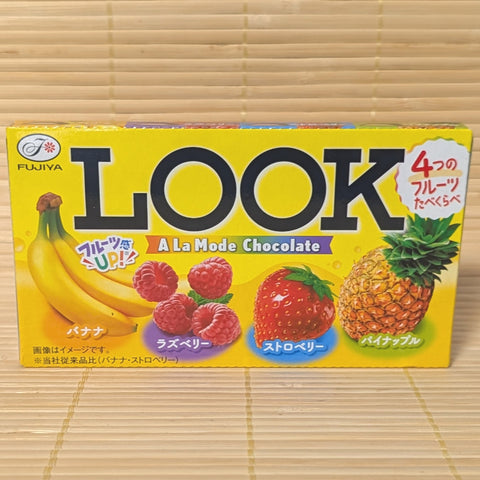 A 46g box of Fujiya LOOK A La Mode chocolate featuring four fruit varieties: Banana, Raspberry, Strawberry, and Pineapple, resting on a bamboo mat.