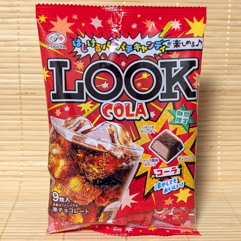 A bright red pop art style bag of Fujiya LOOK Cola chocolates showing an icy glass of cola and a cross section diagram of the popping candy chocolate bite on a bamboo mat background.