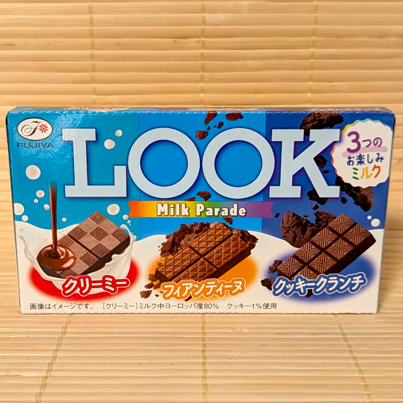 A 43g box of Fujiya LOOK Milk Parade chocolate featuring three varieties: Creamy Milk, Crispy Feuillantine, and Cookie Crunch, resting on a bamboo mat.