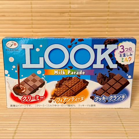 A 43g box of Fujiya LOOK Milk Parade chocolate featuring three varieties: Creamy Milk, Crispy Feuillantine, and Cookie Crunch, resting on a bamboo mat.