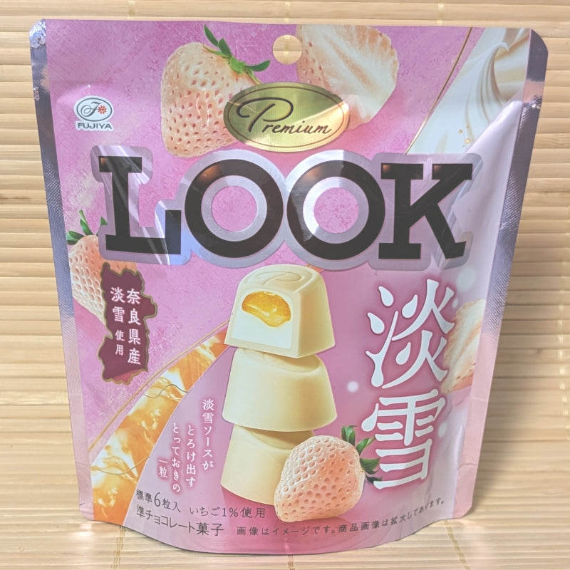 A light pink pouch of LOOK Premium chocolate featuring stacked white chocolate pieces with a flowing strawberry sauce center.