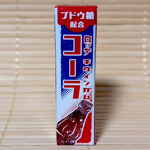 A slim vertical red and blue pack of Lotte Cola Gum with retro Japanese text and a soda bottle illustration. Displayed on a tatami background.