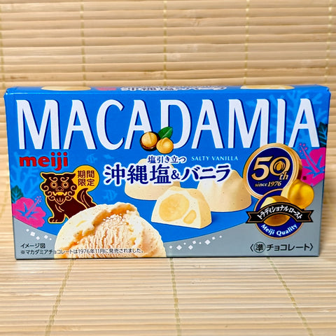 A vibrant blue box of limited edition Meiji Macadamia Okinawa Salty Vanilla chocolate featuring a brown Shisa lion illustration on a tatami background.