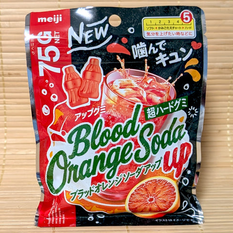 A bold black and red 75g pouch of Meiji Blood Orange Soda Up Gummies showing bottle-shaped gummies and fresh blood orange slices on a bamboo mat.