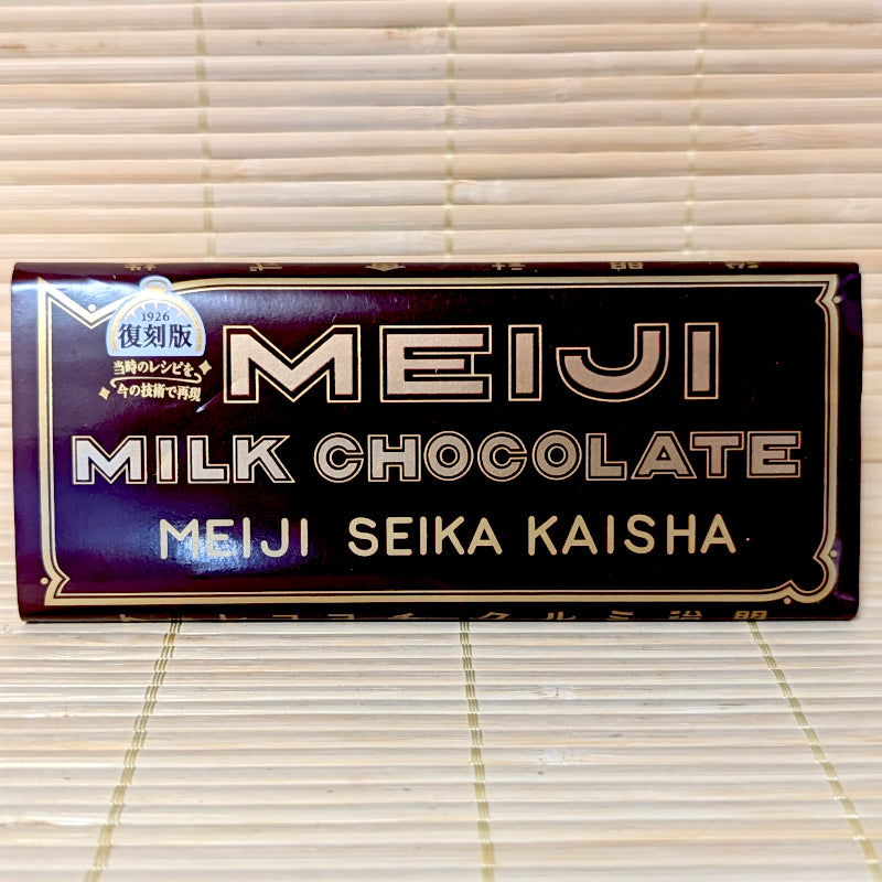 A 40g Meiji Milk Chocolate 1926 Revival Edition bar in vintage brown packaging with gold filigree and original Meiji Seika Kaisha lettering, resting on a bamboo mat.
