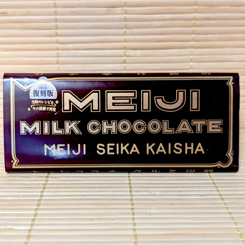 A 40g Meiji Milk Chocolate 1926 Revival Edition bar in vintage brown packaging with gold filigree and original Meiji Seika Kaisha lettering, resting on a bamboo mat.