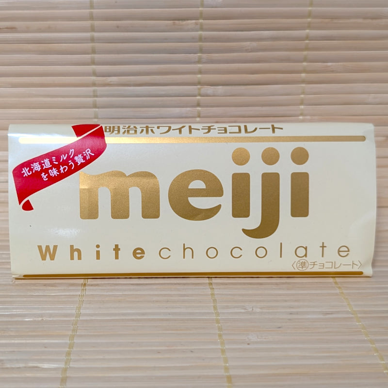 A 40g Meiji White Chocolate bar wrapped in a white paper label with gold lettering, resting on a natural bamboo mat.