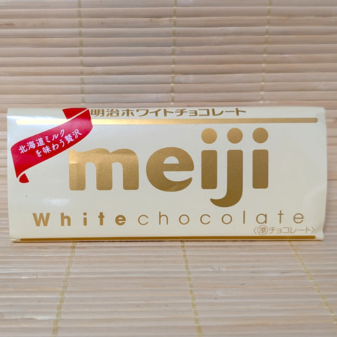 A 40g Meiji White Chocolate bar wrapped in a white paper label with gold lettering, resting on a natural bamboo mat.