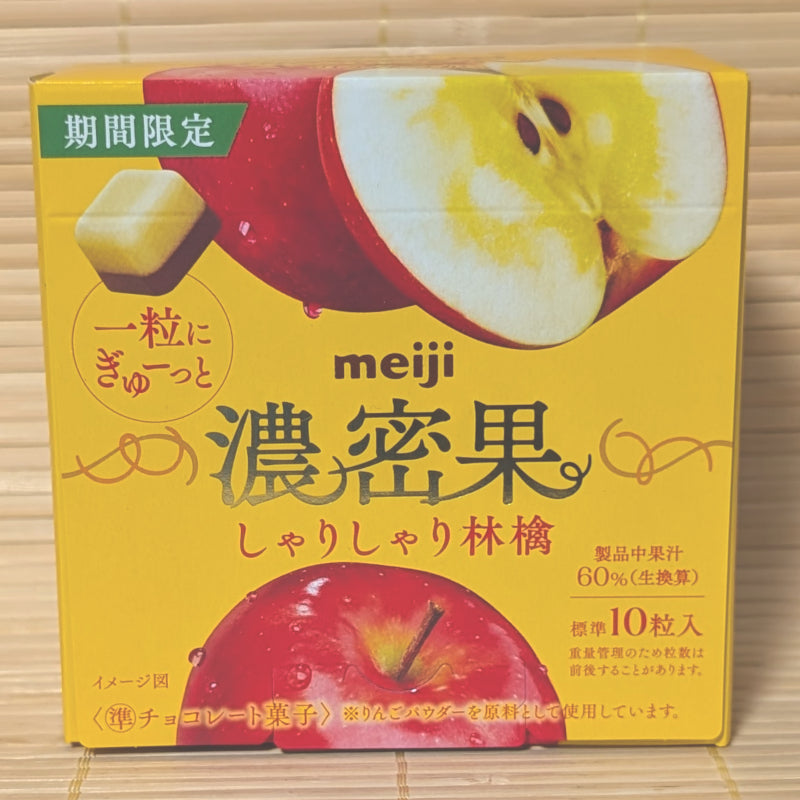 A bright yellow and red 32g box of Meiji Noumitsu Ka Shari Shari Apple chocolates with apple graphics on a bamboo mat.