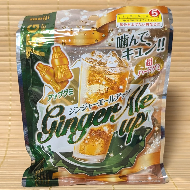 A metallic gold and deep green resealable pouch of Meiji Ginger Ale Up gummies showing a tall glass of sparkling ginger ale on a tatami background.