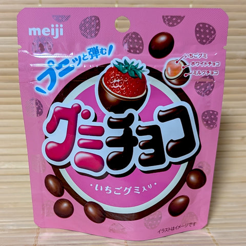 A pink resealable pouch of Meiji Gummy Choco on a tatami background featuring a cross section diagram of the strawberry gummy, mousse, and chocolate layers.
