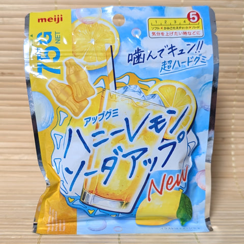 A bright blue and yellow bag of Meiji Honey Lemon Soda-Up gummies showing mini bottle graphics and a tall iced drink on a tatami background.