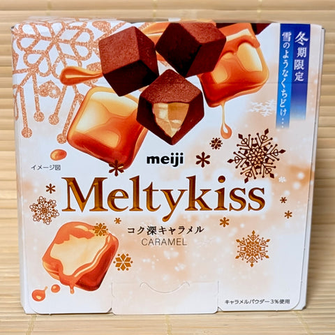 A bronze and white 53g box of Meiji Meltykiss Rich Caramel Chocolate showing caramel graphics and cocoa-dusted cubes on a bamboo background.   