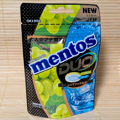 A bright green and blue resealable Mentos pouch showing a cross-section of a green grape and soda-flavored candy. Displayed on a tatami surface.