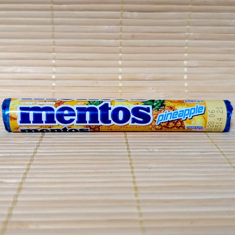 A yellow Mentos roll featuring a blue logo and illustrations of fresh pineapples with Japanese text. Displayed on a tatami surface.