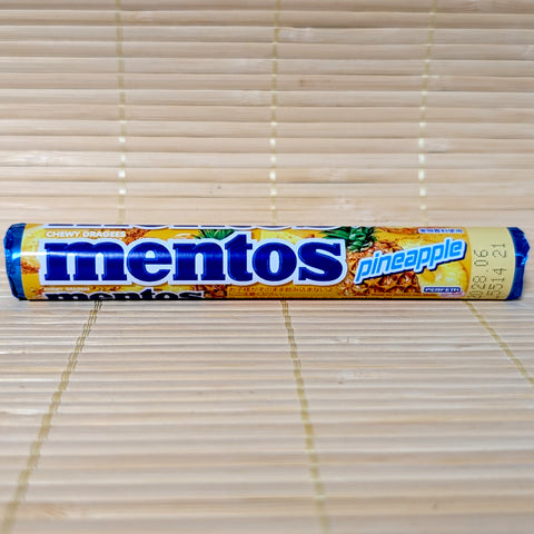 A yellow Mentos roll featuring a blue logo and illustrations of fresh pineapples with Japanese text. Displayed on a tatami surface.